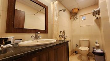 Un baño con tocador de madera, lavamanos, espejo, ducha e inodoro.