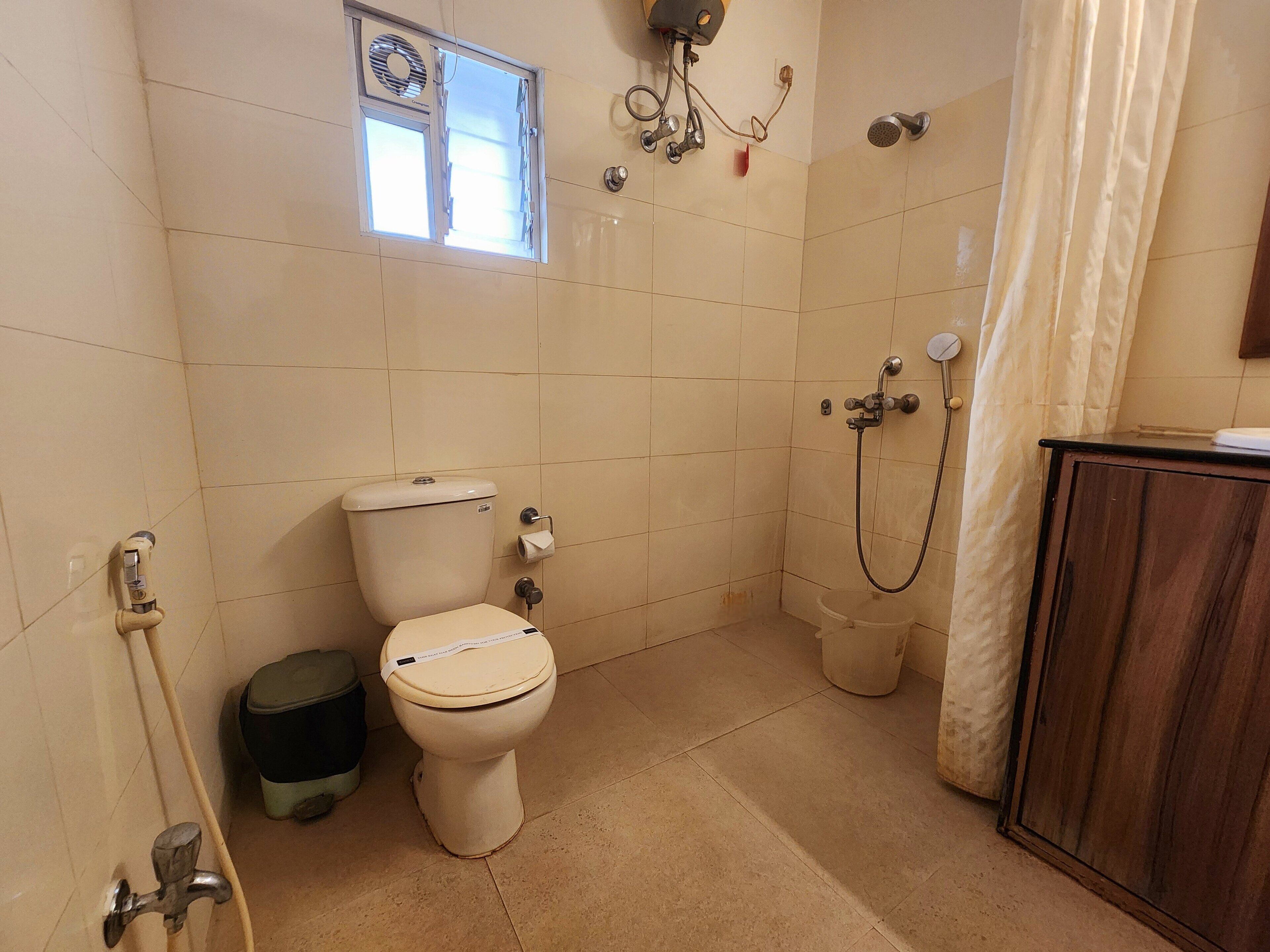 A bathroom with a toilet, a shower, a window, and a cabinet.