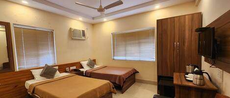 A hotel room with two beds, a ceiling fan, a TV, and a kitchenette.