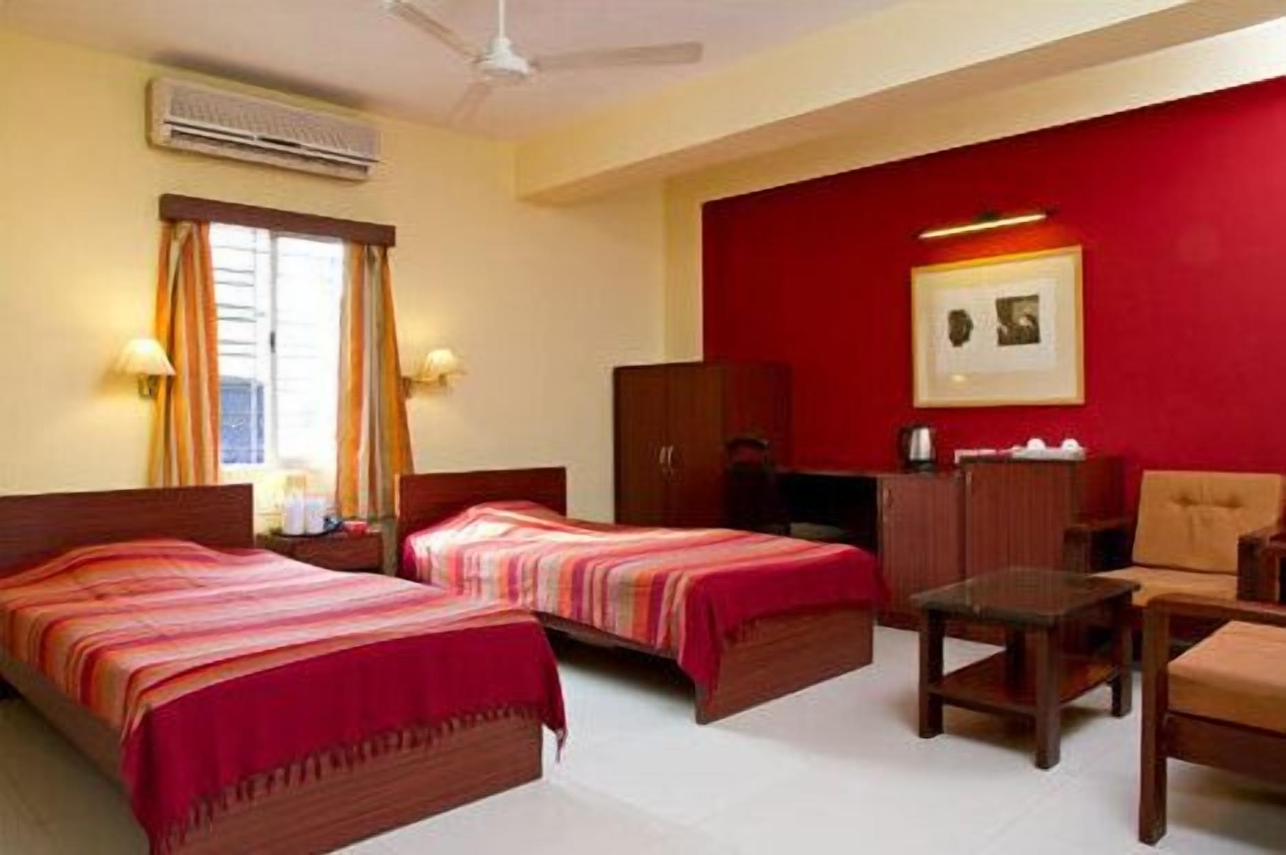 A hotel room with two beds, a desk, a chair, a wardrobe, and a red accent wall.