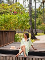 Una mujer sentada en una terraza de madera con un jardín tropical al fondo.