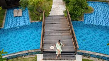 Un pont en bois mène à un espace piscine, d’où l’on a une vue dégagée sur le motif bleu des carreaux de la piscine.