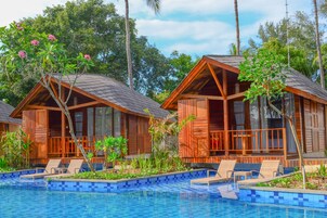 Dos cabañas de madera con balcones, una piscina y vegetación tropical.