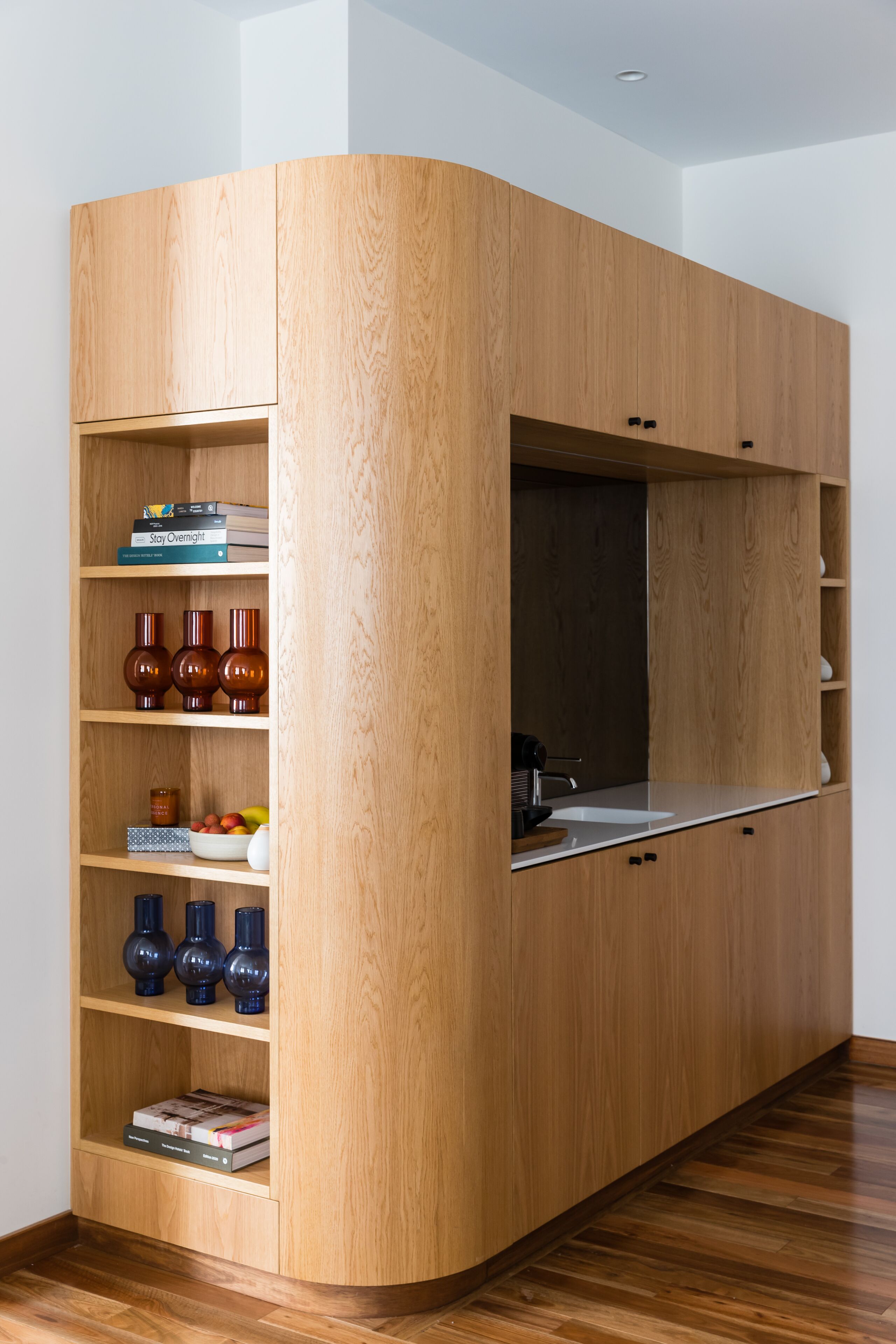 A corner kitchen with wooden cabinetry, a built-in sink, and shelves with decorative items.