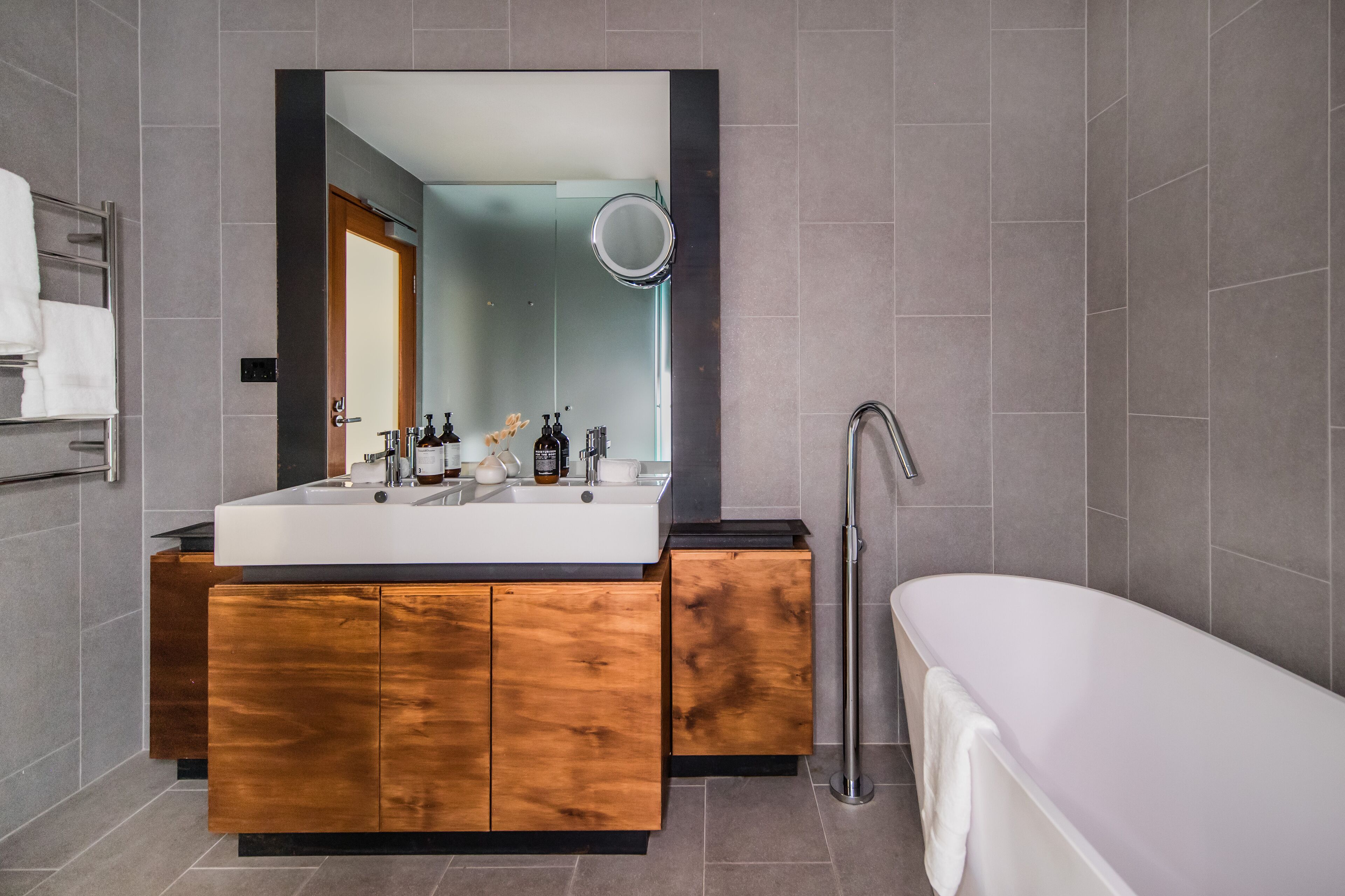 Un baño moderno con un espejo grande, un lavamanos doble, una bañera y un inodoro.