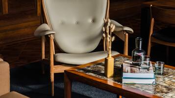 A room with a wooden chair, a small table with a book, a bottle, and a glass.