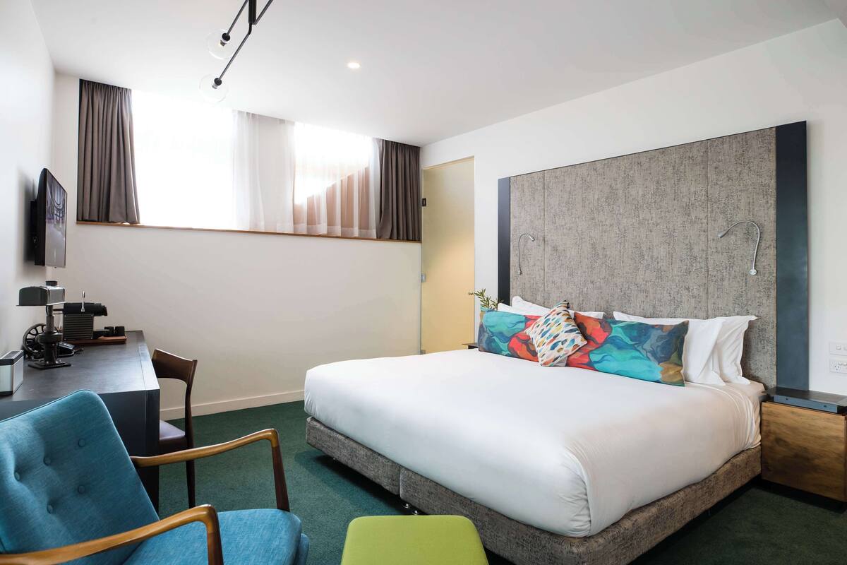 Habitación de hotel con una cama grande, un escritorio con silla, televisor y ventana con cortinas.