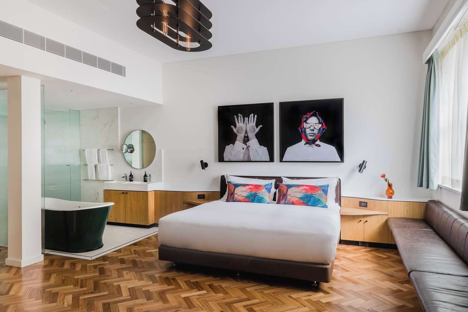 A modern hotel room with a large bed, a sitting area, a vanity with a mirror, and artwork on the walls.