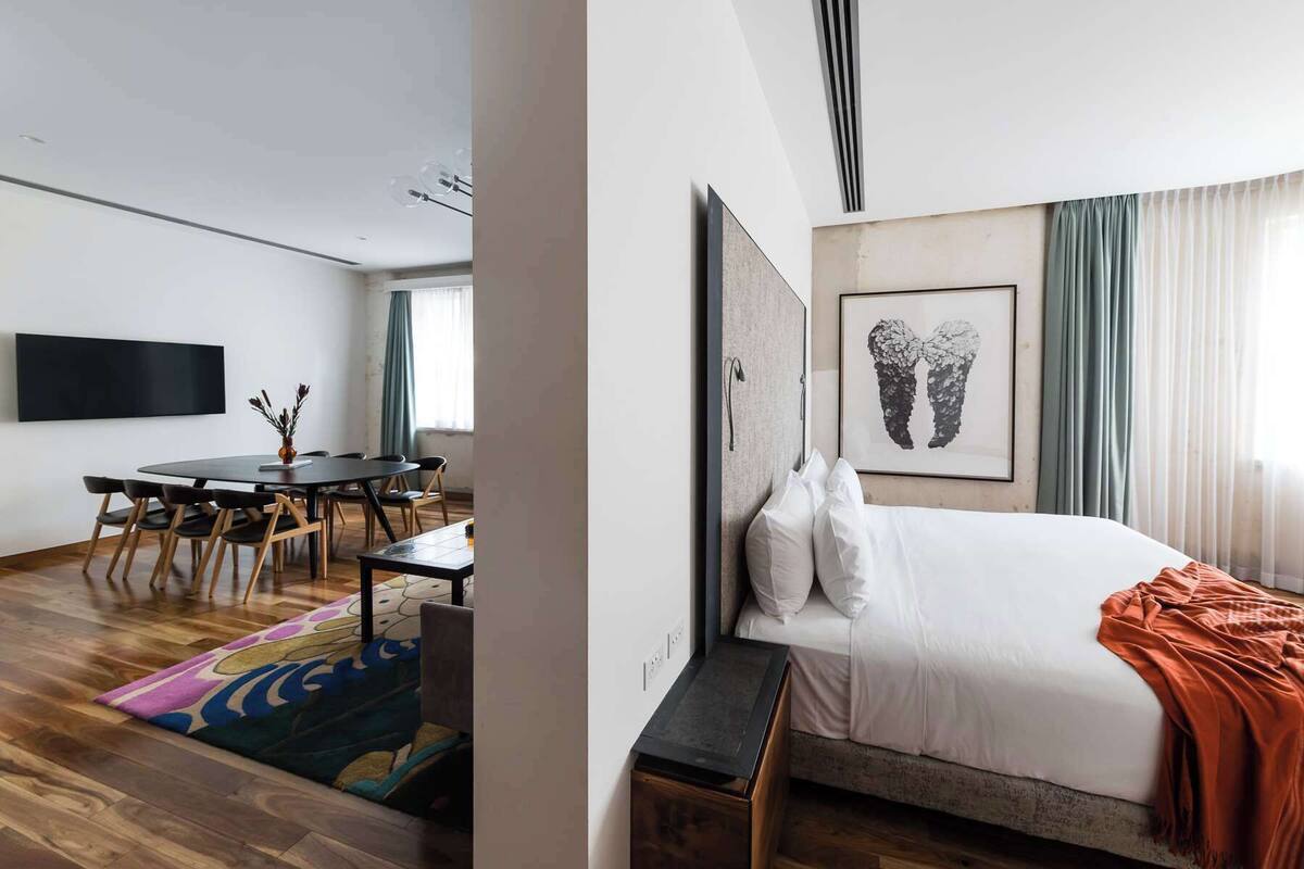 Una habitación de hotel moderna con una cama grande, un escritorio con sillas, un televisor de pantalla plana y una alfombra colorida.
