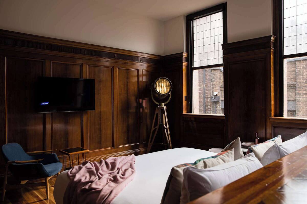 Una habitación de hotel con una cama grande, un escritorio, una silla, un televisor y una lámpara de pie.