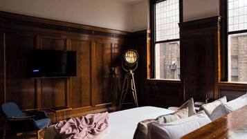 Een hotelkamer met een groot bed, een bureau, een stoel, een televisie en een vloerlamp.