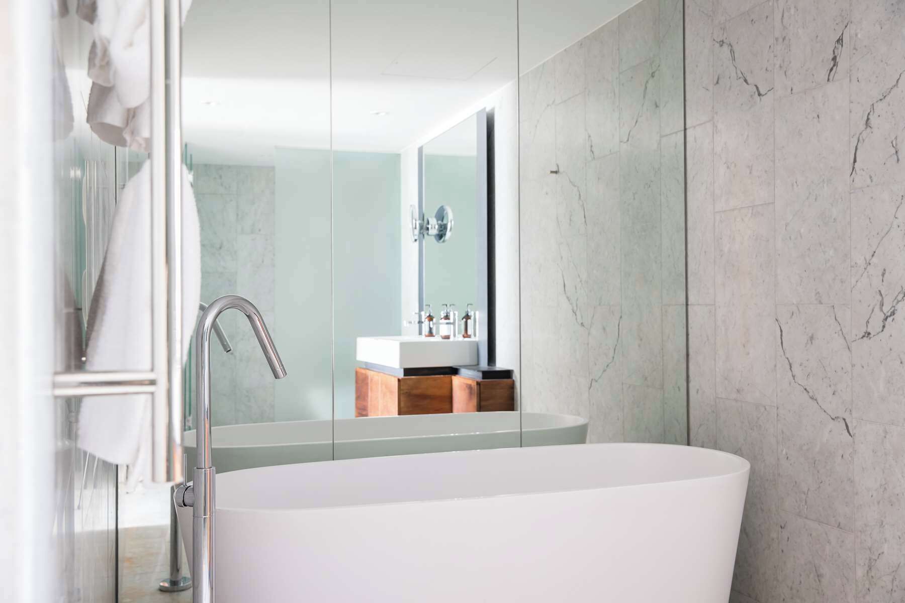 Ein modernes Badezimmer mit einer freistehenden Badewanne, einer Duschkabine aus Glas und einer Marmorwand.