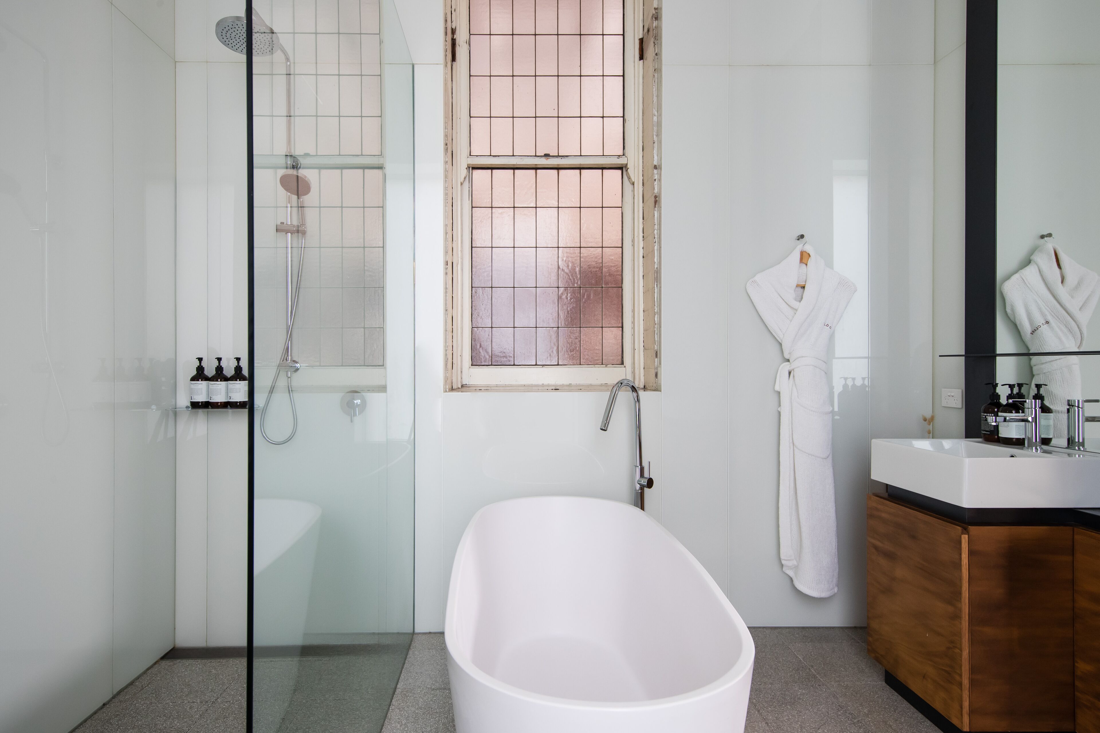 Un baño moderno con ducha de vidrio, una bañera independiente y un mueble de tocador de madera con espejo.