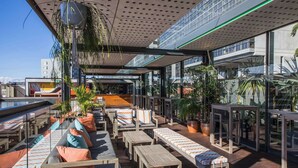 An outdoor lounge area with seating and tables, surrounded by large windows and potted plants. - The Old Clare by Ode Hotels (Chippendale)