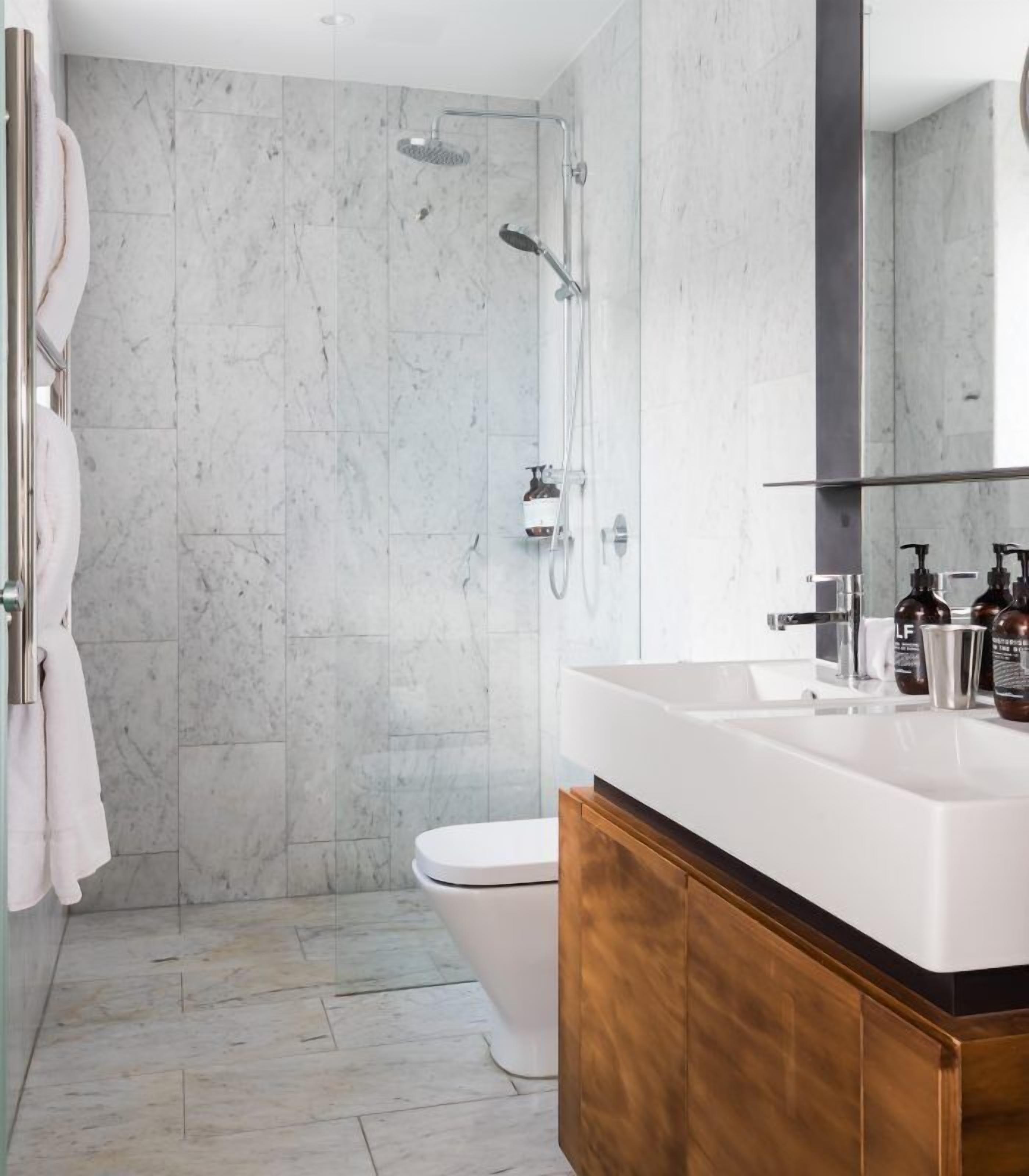 A modern bathroom with a marble shower, a white toilet, and a wooden vanity with a large mirror.