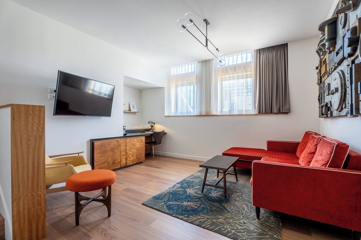 Una sala de estar moderna con un sofá rojo, un aparador de madera, un televisor montado en la pared y una ventana con cortinas.