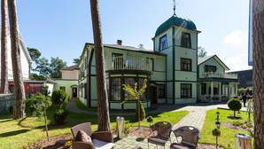 A large, multi-story building with a green and white exterior, a central dome, and a courtyard with outdoor seating. - SUNSET Hotel (Jurmala)