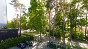 A parking area with several cars, surrounded by trees and a building. - SUNSET Hotel (Jurmala)