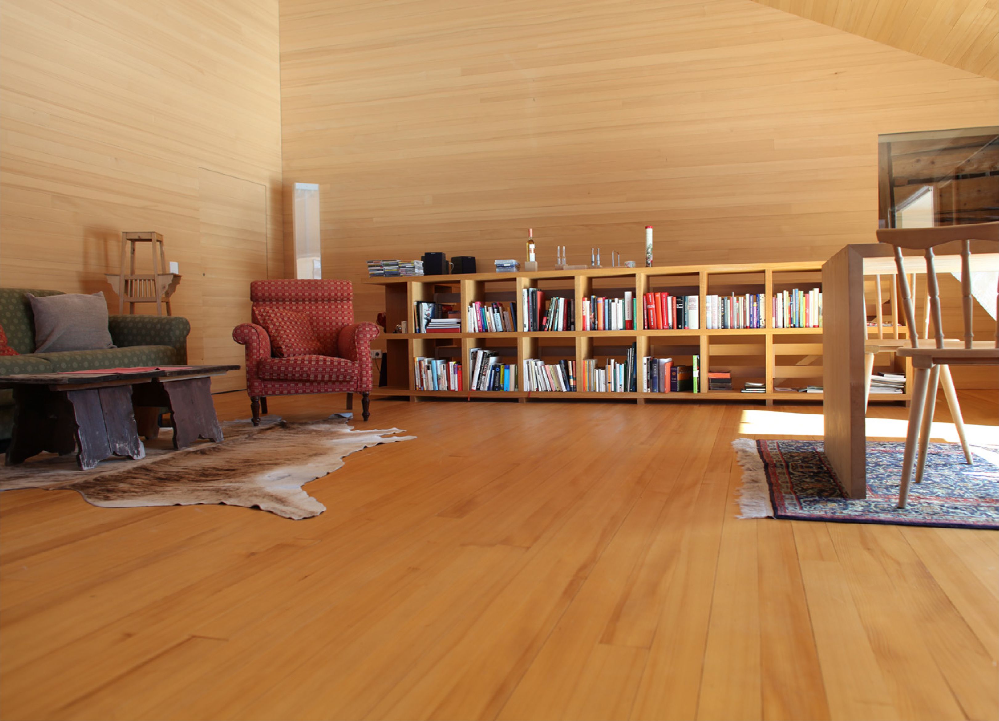 A cozy living room with wooden floors, a red armchair, a sofa, and a bookshelf filled with books.