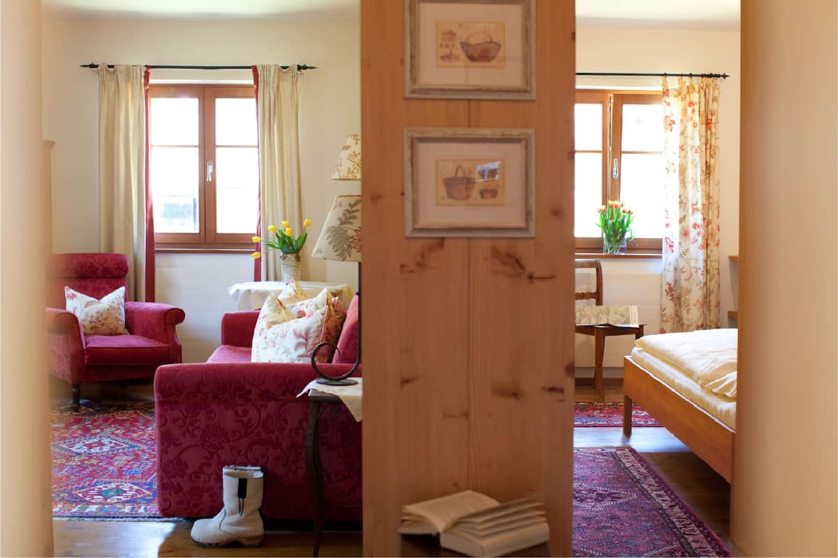 A hotel room with a wooden bed, a red armchair, a sofa, a small table, and a window with curtains.