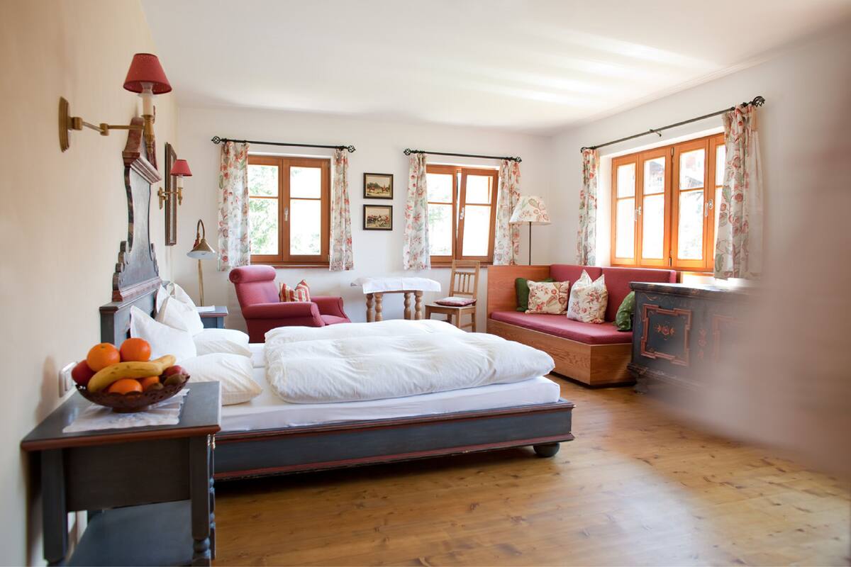 A bedroom with a bed, a bedside table with a fruit bowl, a chair, a small table, and a sofa.