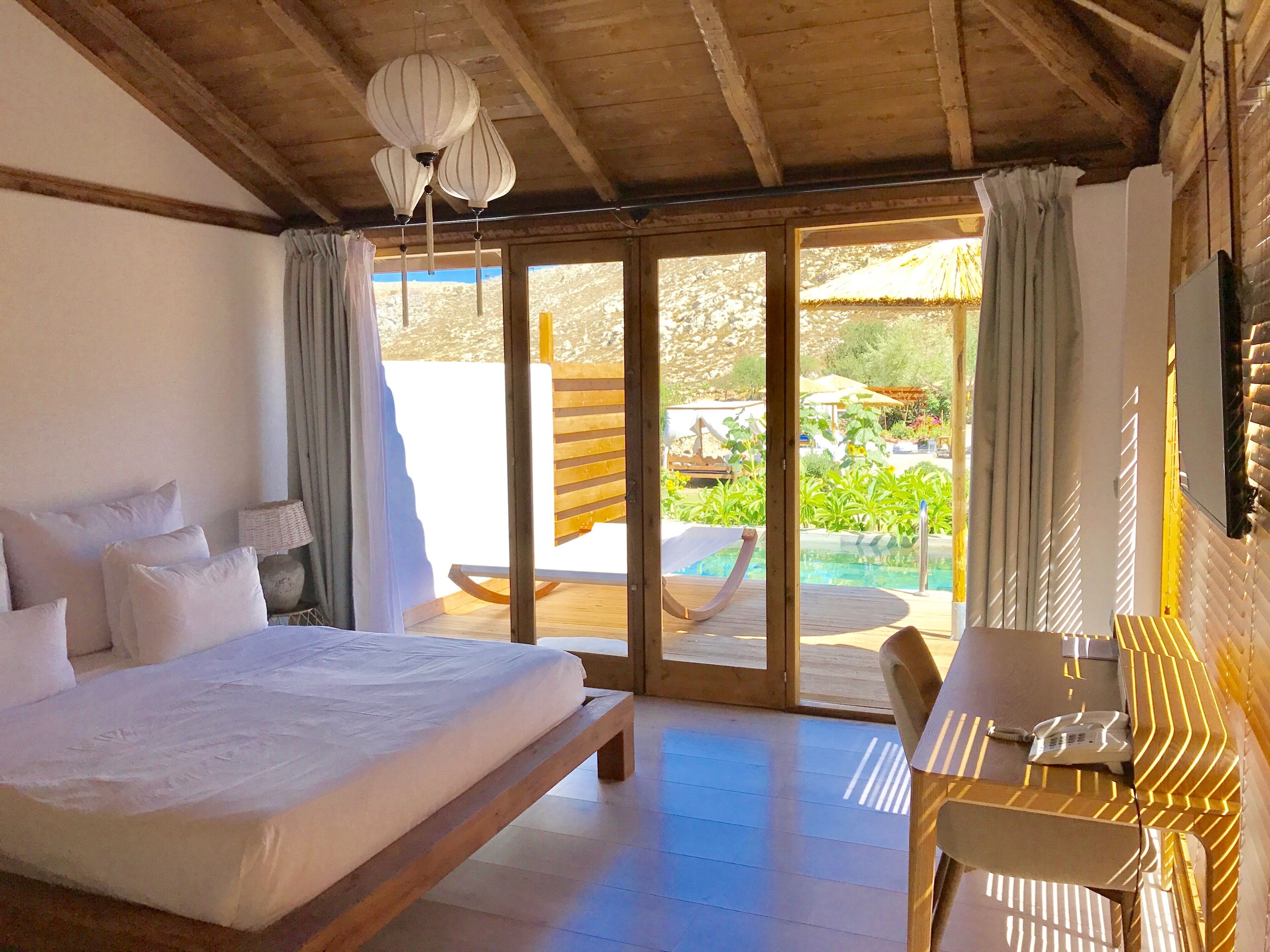 Een slaapkamer met een groot bed, een bureau en uitzicht op een zwembad en tuin.