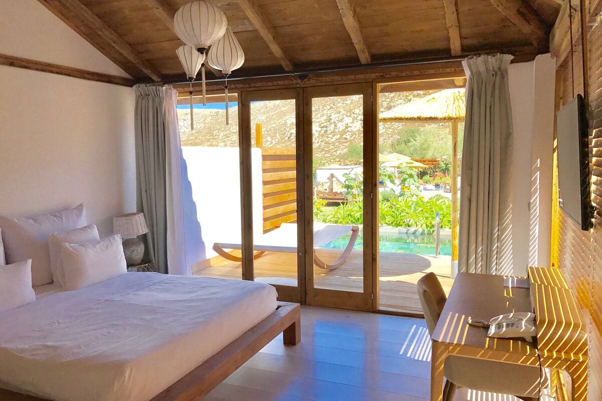 Een slaapkamer met een groot bed, een bureau en uitzicht op een zwembad en tuin.