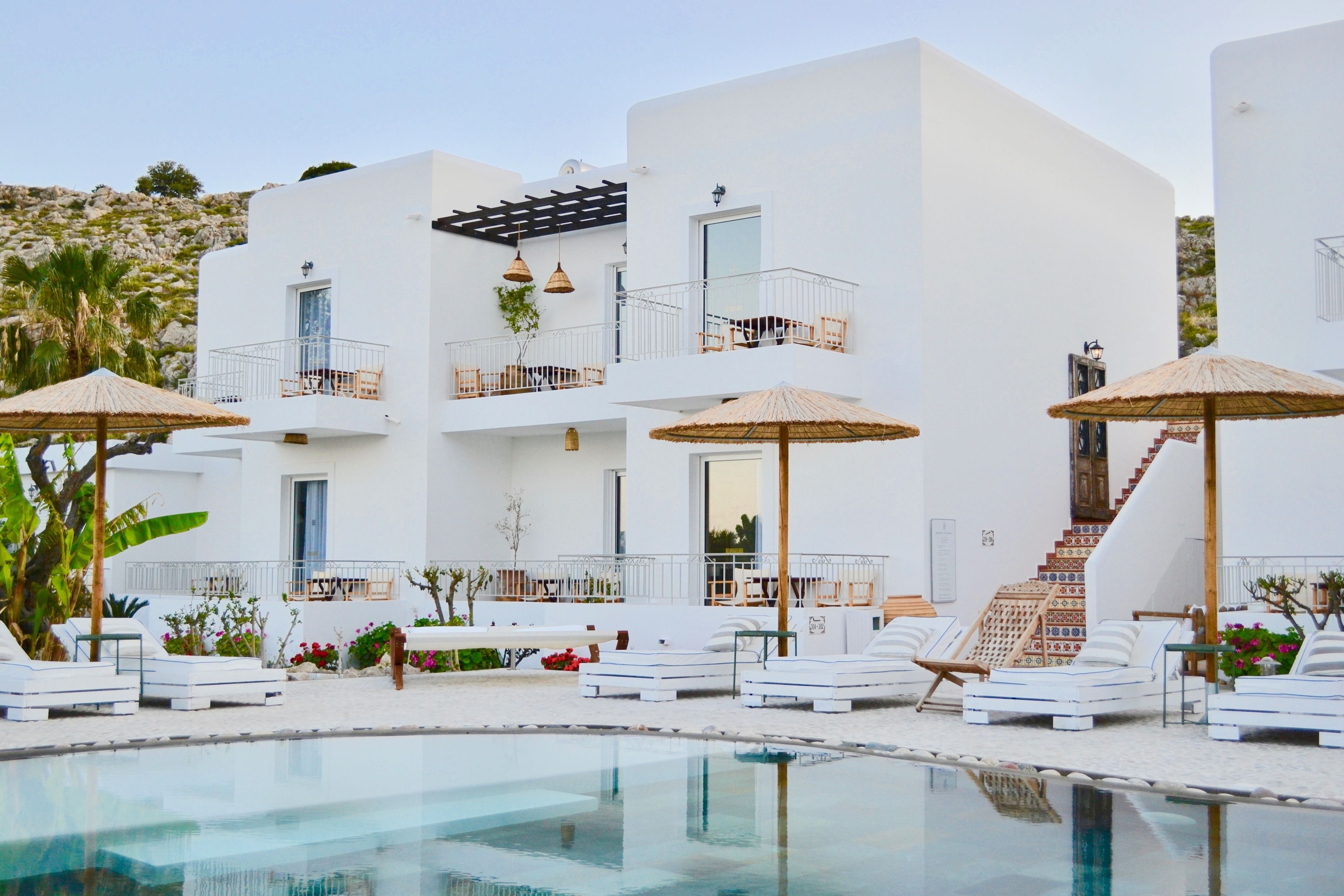 Un edificio moderno blanco con piscina, tumbonas y sombrillas.