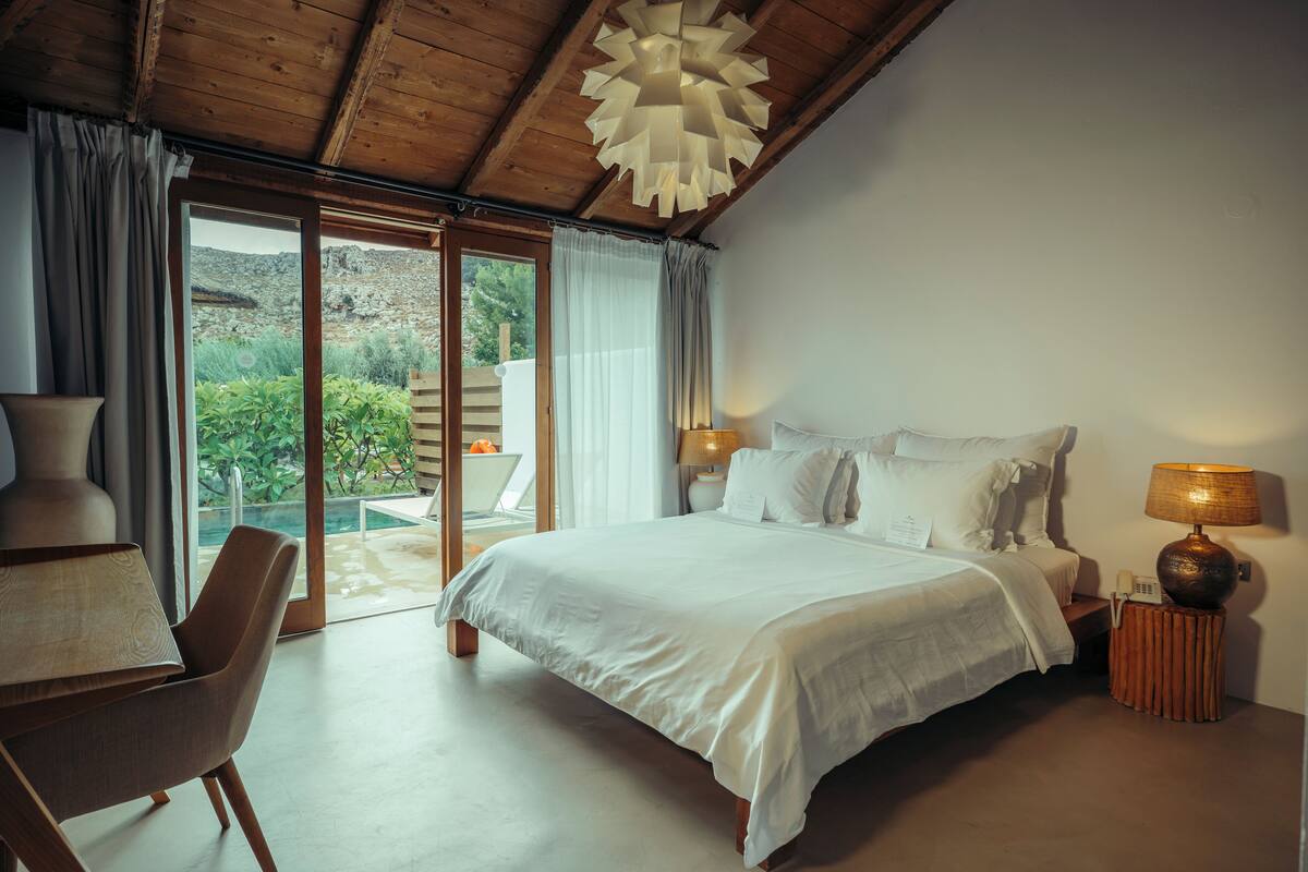 Een slaapkamer met een bed, een bureau, een stoel, een lamp en uitzicht op de omgeving.