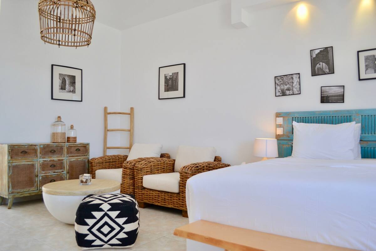 Een slaapkamer met een bed, rieten meubels, een ronde tafel en een dressoir.