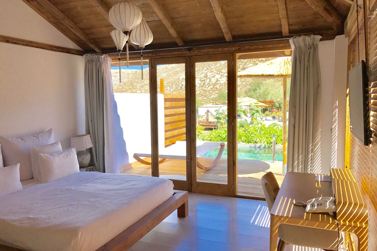 A bedroom with a large bed, a desk, and a view of a pool and garden.