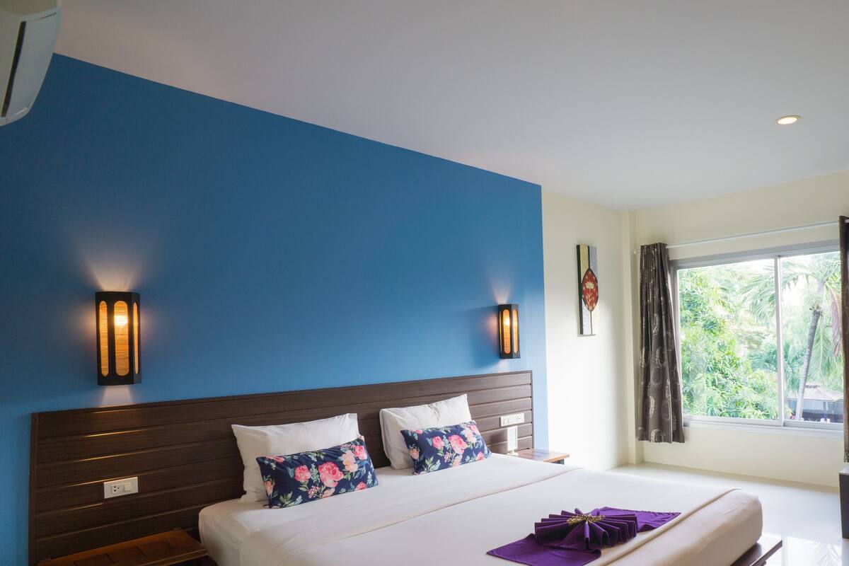 Ein Hotelzimmer mit einem großen Bett, zwei Wandlampen, einem Fenster mit Vorhängen und einem kleinen Tisch.
