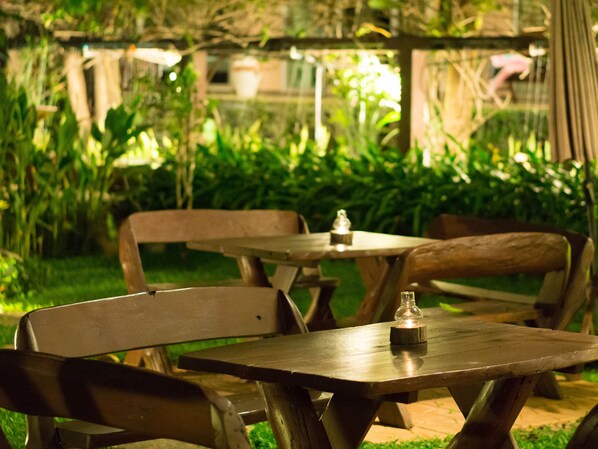 An outdoor wooden table and chairs set in a garden with lush greenery and a pergola structure in the background.