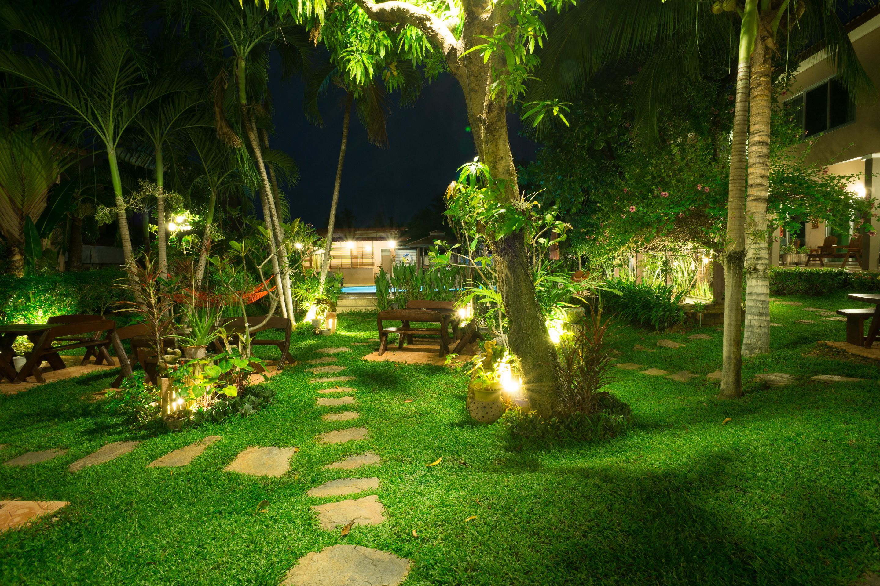 Un jardín al aire libre bien iluminado con senderos de piedra, bancos y abundante vegetación.