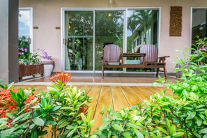 Una terraza de madera con sillas y plantas en macetas, una puerta corrediza de vidrio y un adorno montado en la pared.