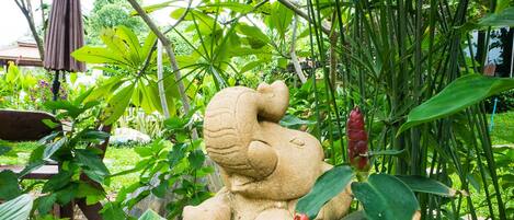 A garden with a stone statue of a seated figure surrounded by lush greenery and a wooden stump.