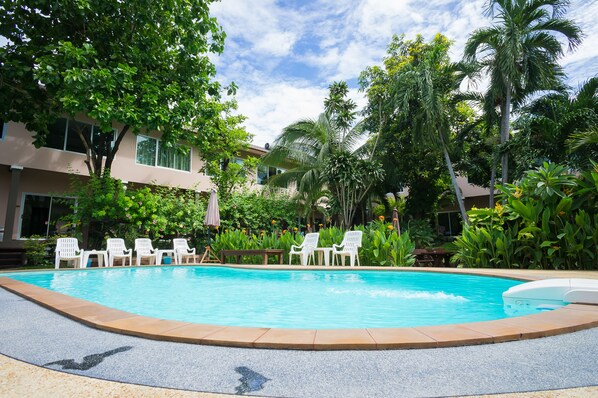 Una piscina con sillas blancas y una palmera al fondo.