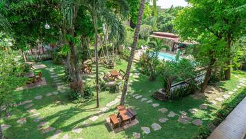 A lush garden with a pool, stone pathways, and wooden furniture.