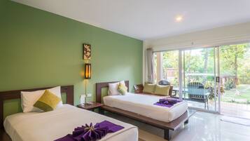 A hotel room with two beds, a green wall, a window with a view of the garden, and a small table with a chair.