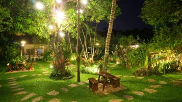 A well-lit garden with a wooden bench, stone pathway, and lush greenery.