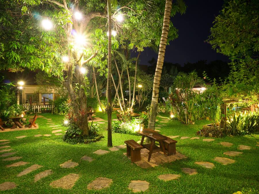 A well-lit garden with a wooden bench, stone pathway, and lush greenery.