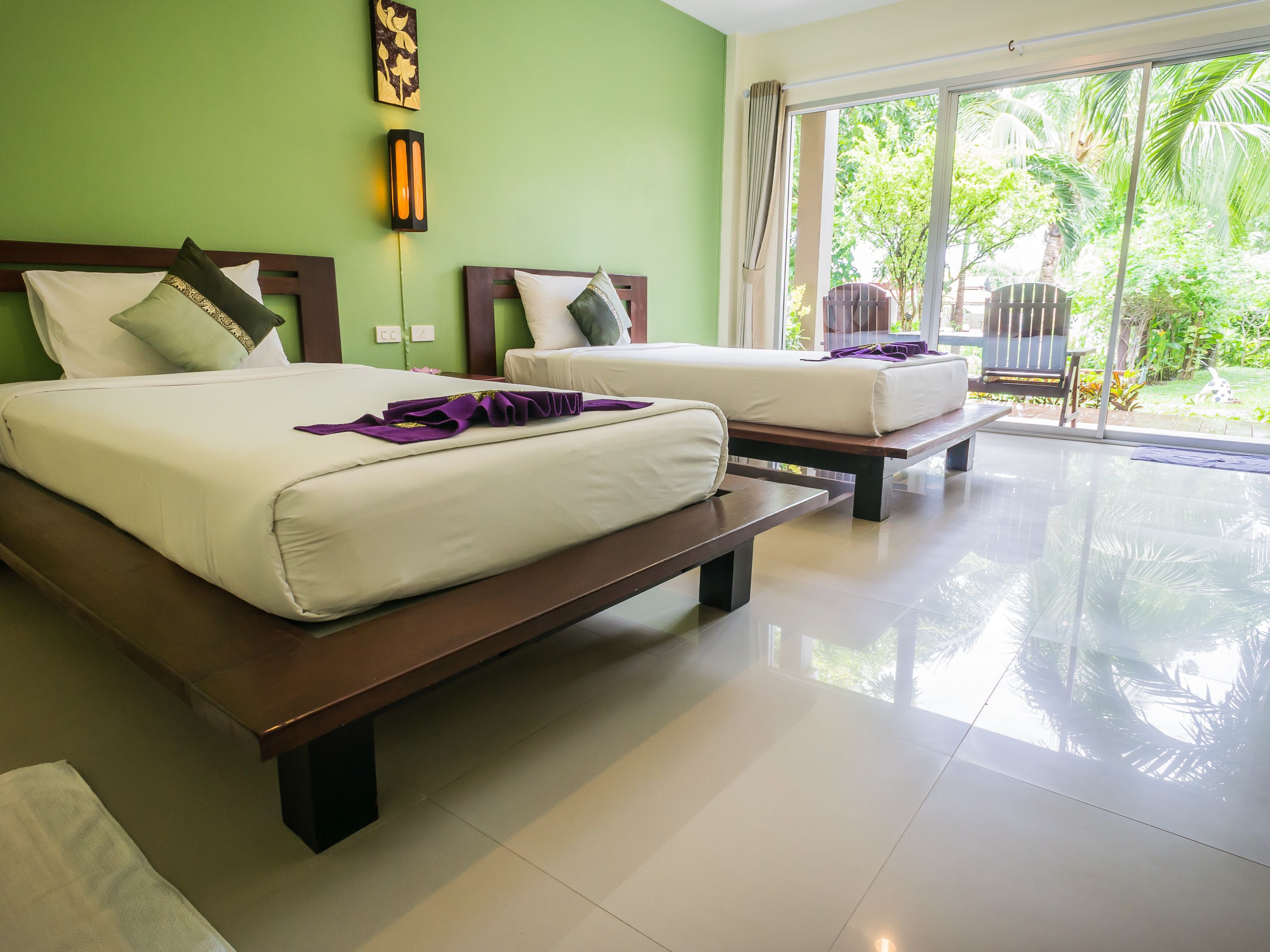 A hotel room with two beds, a large window, and a view of greenery outside.