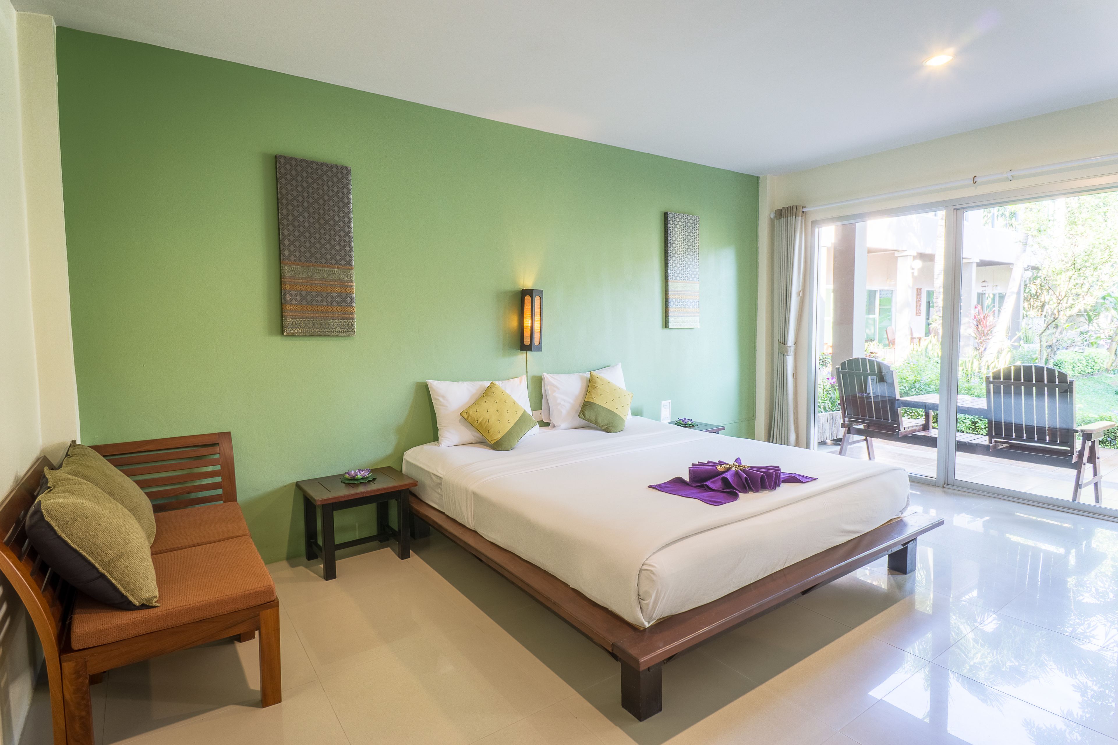 A bedroom with a bed, a wooden bench, a nightstand, and a view of the outside through a sliding glass door.