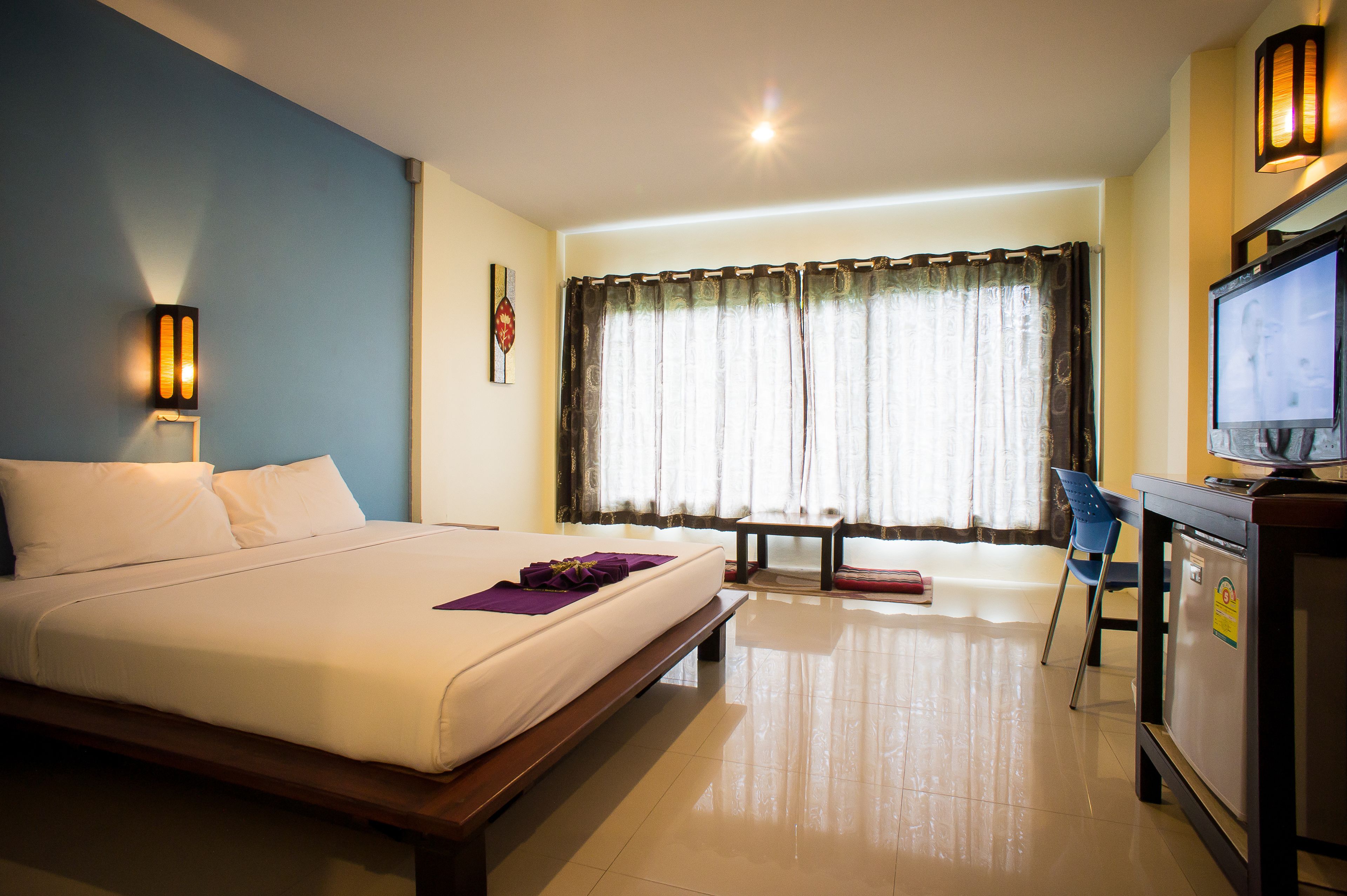 A hotel room with a bed, a desk with a television, a chair, and a window with curtains.