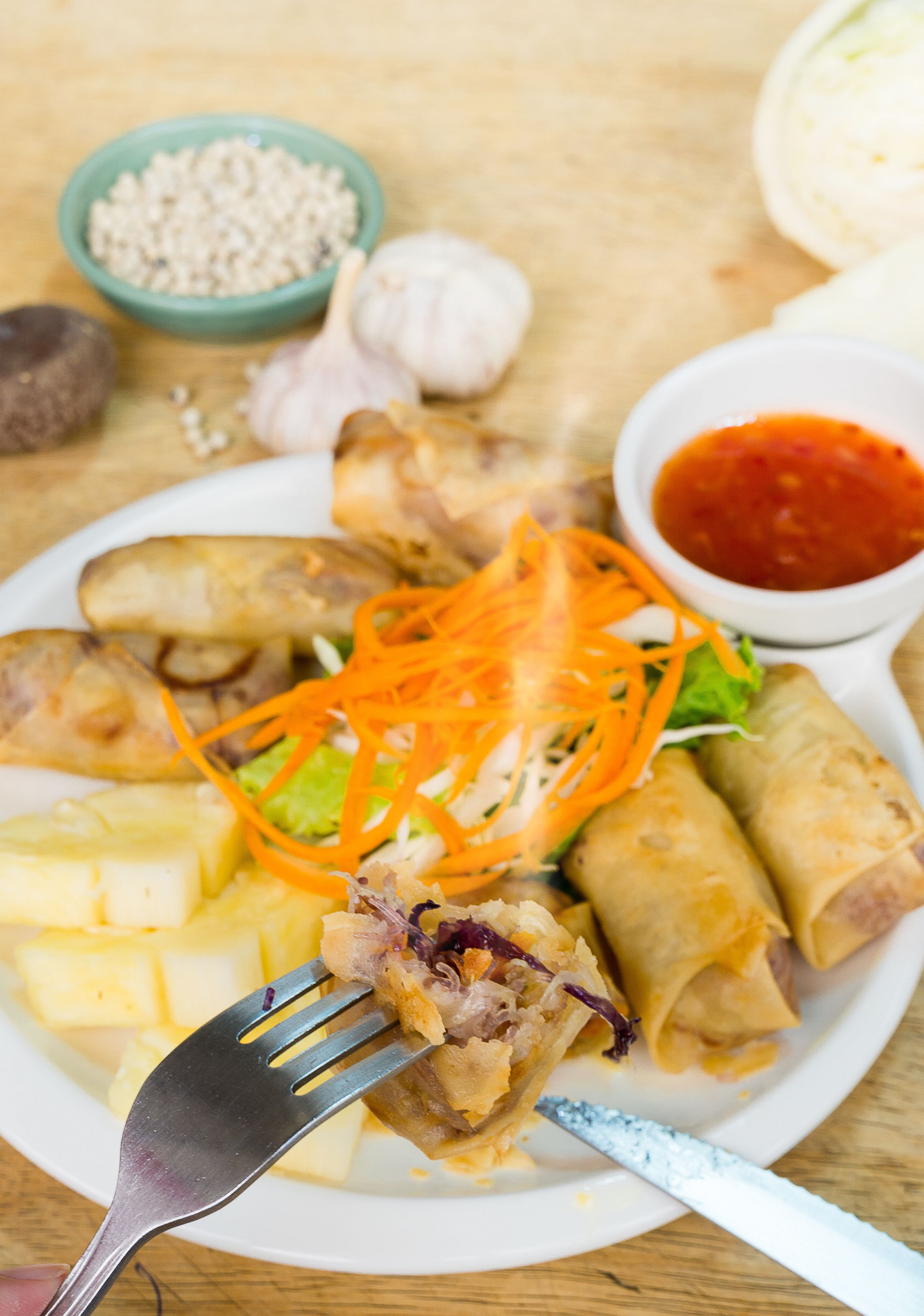A plate of spring rolls, a bowl of sauce, and some vegetables on a wooden table.