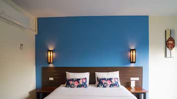 Une chambre d’hôtel avec un mur d’accent bleu, une tête de lit en bois, deux lampes de chevet, un coussin à motifs floraux et une petite œuvre d’art accrochée au mur.