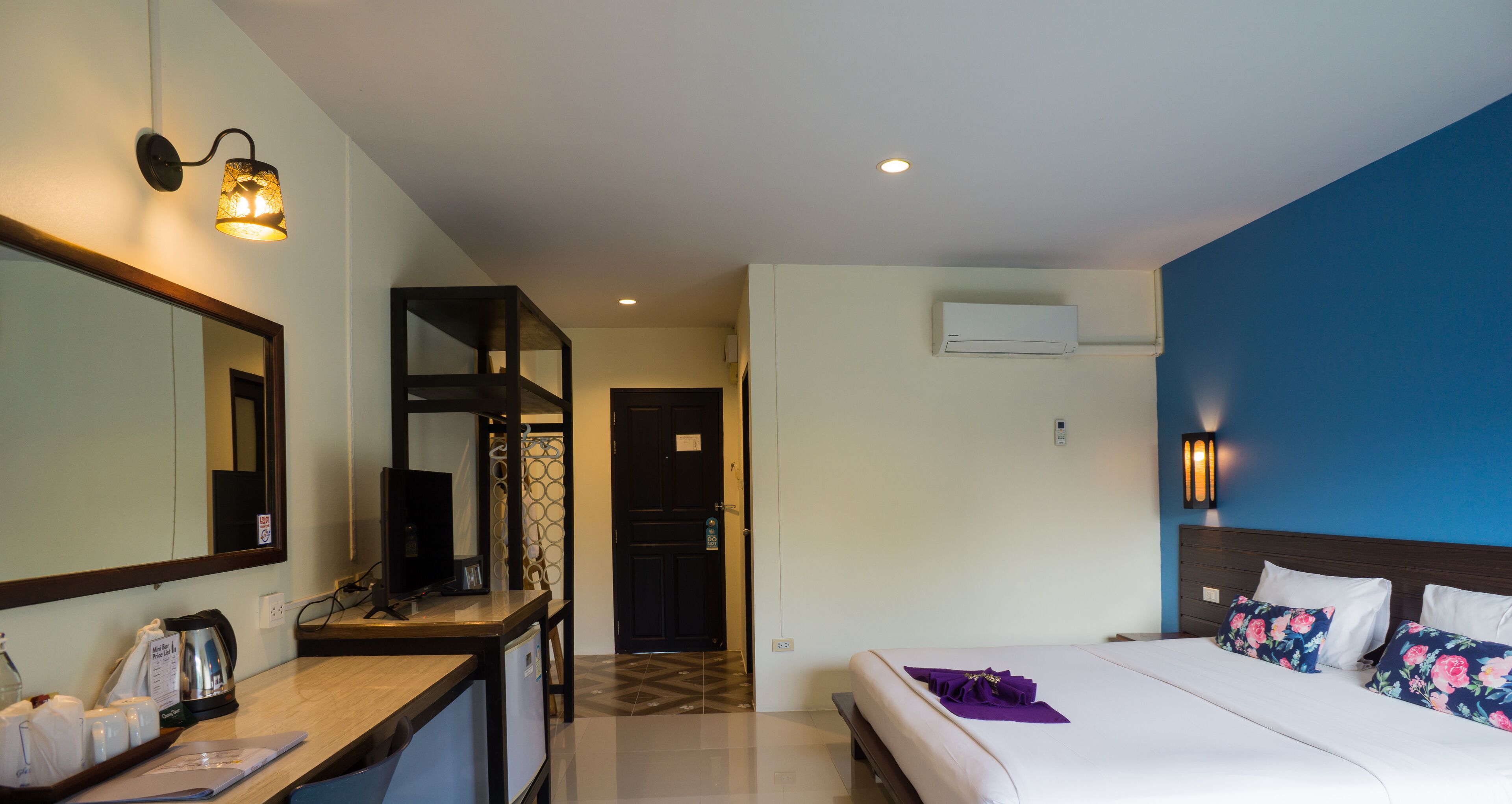 A hotel room with a bed, a desk with a coffee maker, a mirror, and an air conditioning unit.