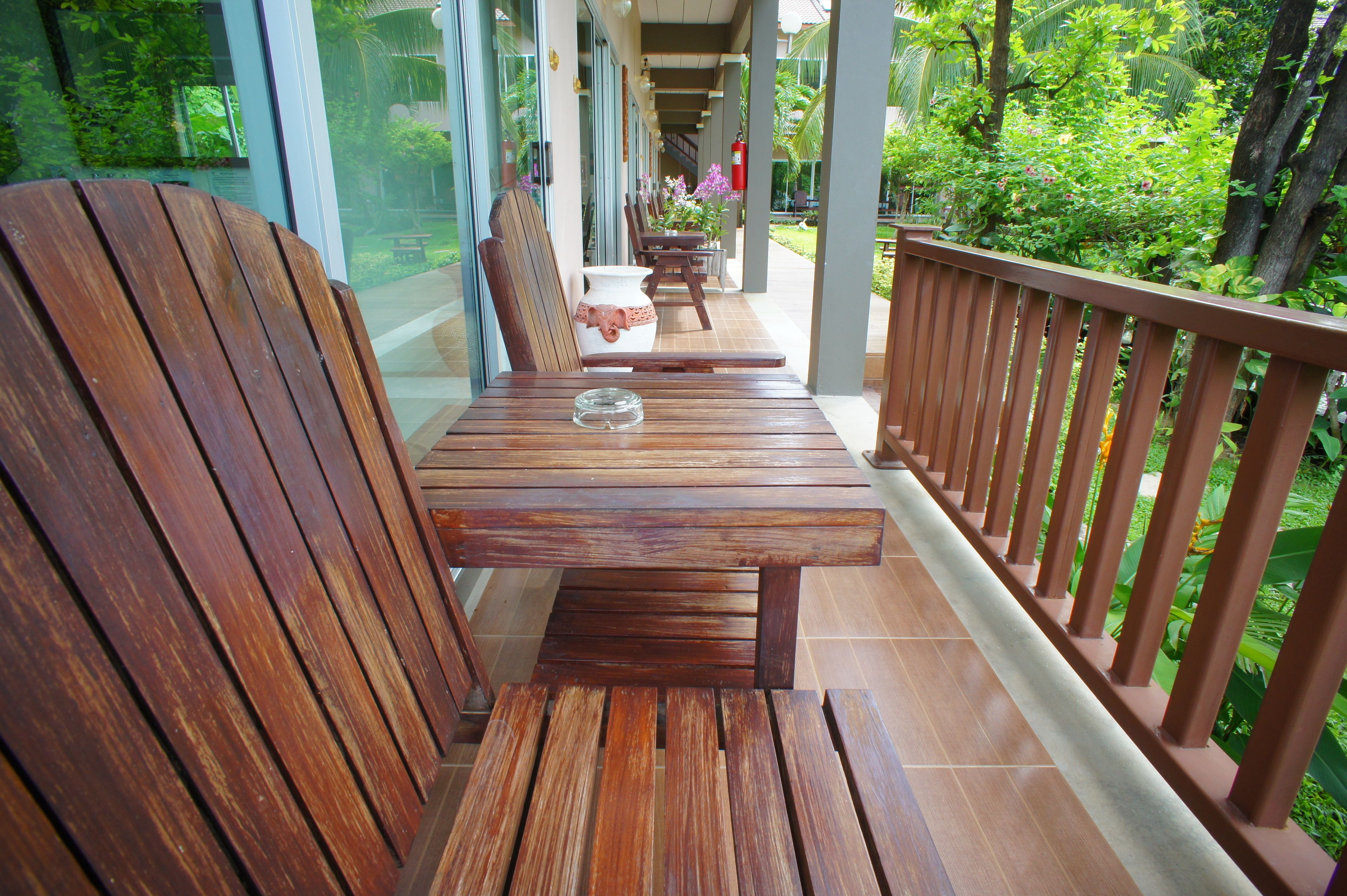 Un banco de madera y una mesa en un porche cubierto, con vista a un jardín exuberante.