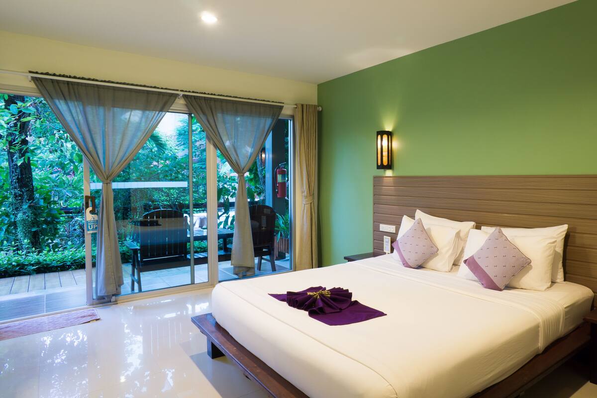 Ein Hotelzimmer mit einem großen Bett, Blick auf einen Garten und einer Schiebetür.