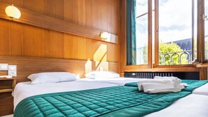 A hotel room with a wooden headboard, a large bed with a green quilt, white pillows, and a view of greenery outside. - Hôtel Bristol Metz Centre Gare (Metz)